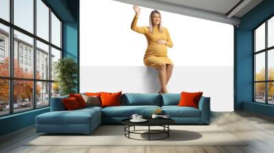 Full length portrait of a pregnant woman in a yellow dress sitting on a blank panel and waving Wall mural