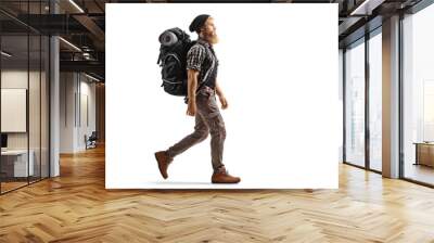 Full length profile shot of a young bearded man with a backpack and hiking equipment walking Wall mural