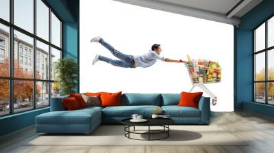 Full length shot of a casual young man flying with a shopping cart with food Wall mural