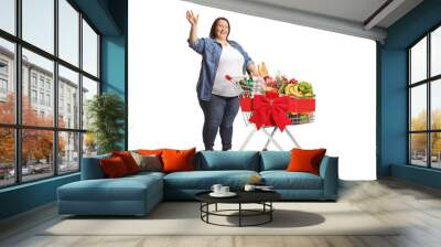 Full length shot of a chubby woman standing with a full shopping cart and waving Wall mural