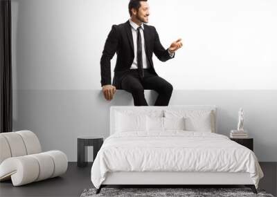 Handsome young man in a suit sitting on a blank panel and gesturing with hand Wall mural