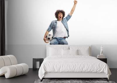 Happy young man cheering and holding a football seated on a blank panel Wall mural