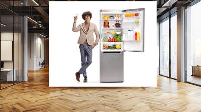 Happy young man pointing up and standing next to a fridge Wall mural