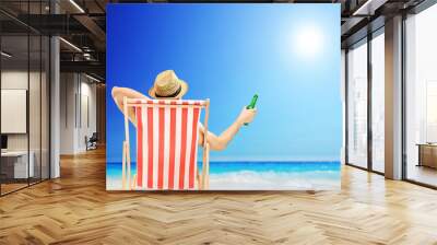 Man with hat sitting on a beach chair and holding a beer Wall mural