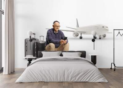 Mature man sitting on a suitcase waiting for a flight and using a smartphone Wall mural