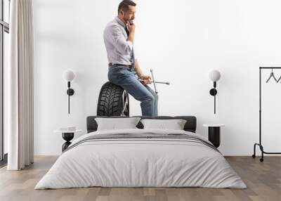 Profile shot of a pensive man sitting on a car tire and holding a lug wrench Wall mural