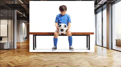 Sad little footballer seated on a wooden bench Wall mural