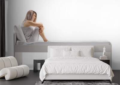 Sad young woman in pajamas sitting on a bed and thinking Wall mural