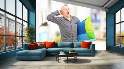 Sleepy mature man in pajamas holding a pillow and yawning at hom Wall mural