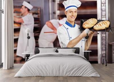 Smiling male baker posing with freshly baked breads in bakery Wall mural