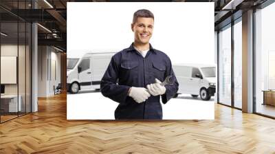 Smiling mechanic worker holding a wrench and standing in front of two white vans Wall mural