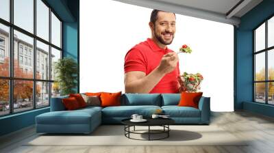 Smiling young man eating a healthy fresh salad in a bowl Wall mural