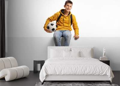 Teenager boy holding a soccer ball and sitting on a white panel board Wall mural