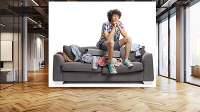 Tired young man sitting on top of a suitcase on a sofa Wall mural