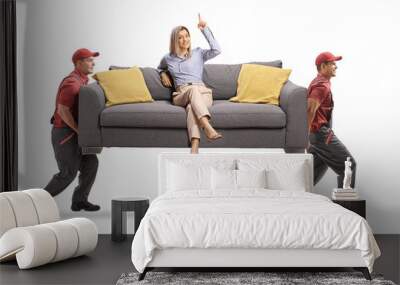 Woman sitting on a sofa and pointing up while two workers from a removal company carry the sofa Wall mural