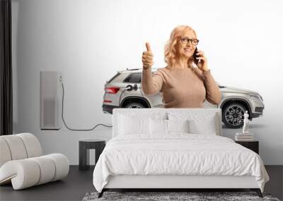 Woman using a smartphone and standing in front of a SUV at electric charging point Wall mural