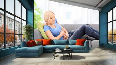 Woman with stomach pain sittin on sofa Wall mural