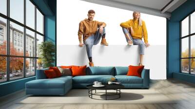 Young casual trendy man and woman sitting on a blank panel Wall mural