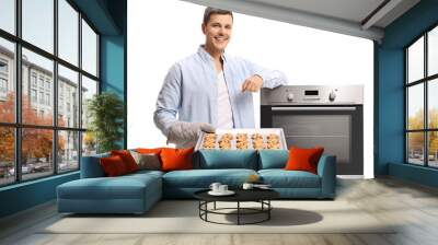 Young man holding a tray of freshly baked cookies and leaning on an oven Wall mural