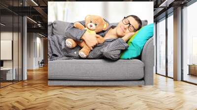 young man holding teddy bear and taking a nap on couch Wall mural