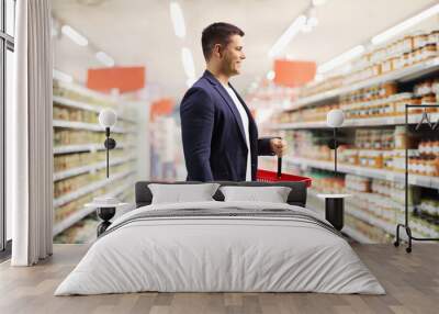 Young man in a supermarket carrying a red shopping basket Wall mural