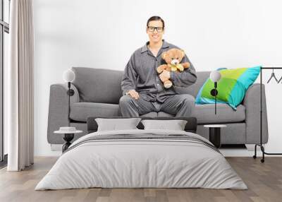 young man in pajamas sitting on sofa with teddy bear Wall mural