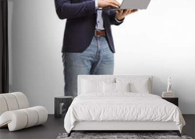 Young man in suit and jeans standing with an open laptop computer and working Wall mural