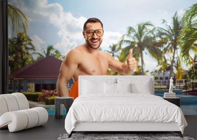 Young man in swimwear holding a plastic flying disc and gesturing thumbs up by the pool Wall mural