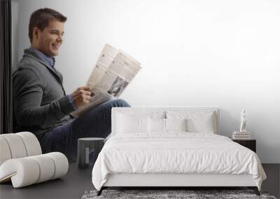 Young man seated on the floor reading a newspaper and leaning against a wall Wall mural