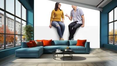 Young man sitting on a blank signboard and talking to a young woman Wall mural