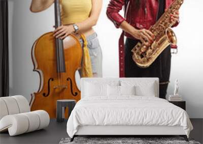 Young trendy female musicians with a cello and a sax posing and looking at camera Wall mural