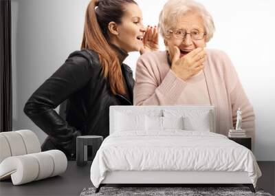 Young woman whispering to a surprised senior woman Wall mural