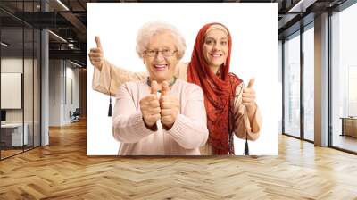 Young woman with a head scarf behind an elderly woman showing thumbs up Wall mural