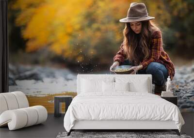 photography young gold prospector female dressed in modern outdoor gear crouching and panning for gold focused expression water splashing around pan clear river with gravel bed vibrant autumn foliage Wall mural