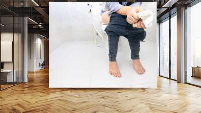 Women are using public restrooms. Young woman sitting on toilet bowl holding tissue paper. Wall mural