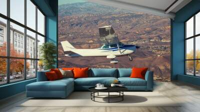 Small airplane flying in the sky over the mountains Wall mural