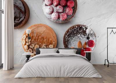 Delicious tarts with caramel and hazelnuts, with dark chocolate, raspberries, almond and powdered sugar on the light colored background. Top view, flat lay, natural light. Copy space Wall mural