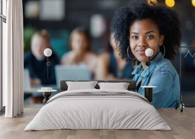 Attractive African young confident businesswoman sitting at the office table with a group of colleagues in the background, working on a laptop computer. This scene captures professionalism, teamwork Wall mural