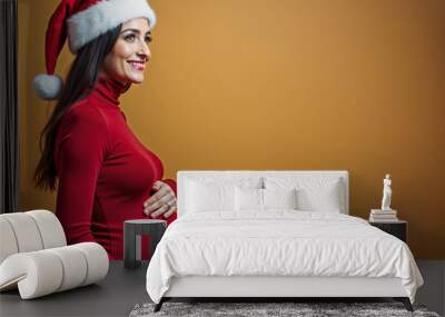 portrait of a pregnant caucasian woman in santa claus clothes and hat on a orange background Wall mural