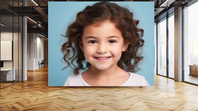 happy little girl with long curly hair over blue background, looking at camera Wall mural