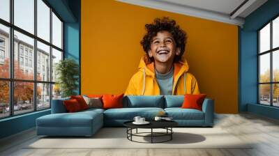 Portrait of a smiling little boy in yellow jacket over yellow background Wall mural