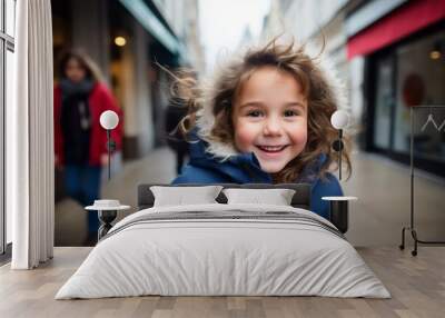 Portrait of smiling little girl in blue coat on the street. Wall mural