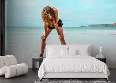 Athletic young woman resting after running on beach Wall mural