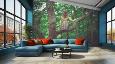 Young woman sitting in tree in the forest Wall mural