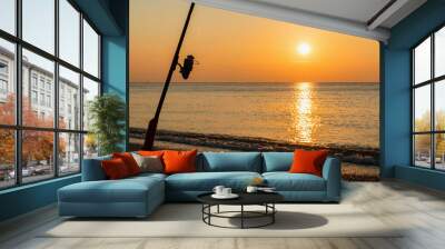 fishing on the calm sea from the beach. Panorama with sunrise and fishing rod set on the sand Wall mural