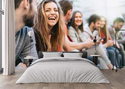 Group of trendy young people chatting together sitting on a bench outdoors. Students having fun together. Focus on a blonde girl smiling with open mouth Wall mural