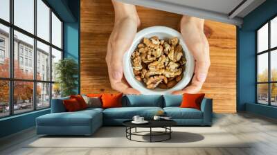 Healthy nut mix in ceramic bowl held by woman hands on wooden table, walnut almond snack Wall mural