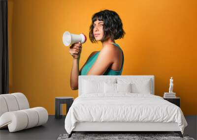 Pretty European woman wearing a teal tank top talking loud on a megaphone against an orange background Wall mural