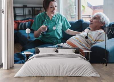 Smart wristband for assisted living - Nurse explains the operation of the smartwatch to an elderly patient lying on the sofa. Wall mural