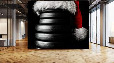 Heavy dumbbells weight plates stacked on top of each other in the shape of a snowman, with red Santa Claus hat. Healthy fitness lifestyle Christmas concept. Wall mural